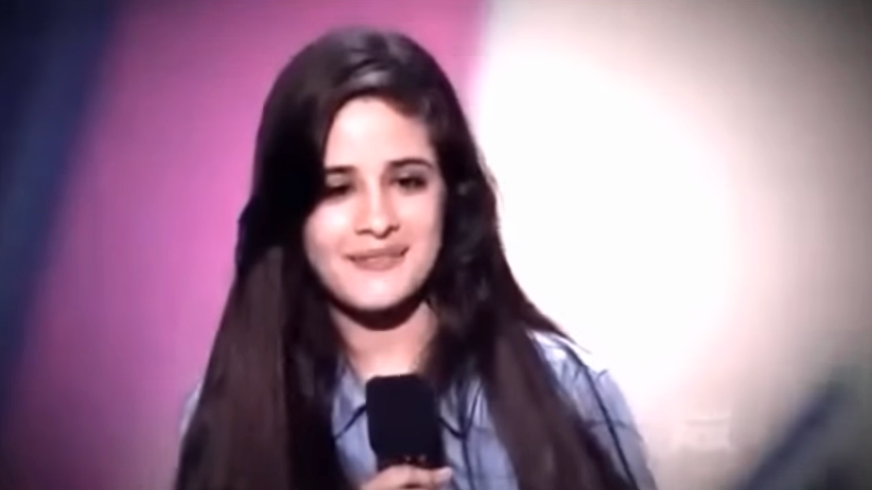 A idiosyncratic with agelong hairsbreadth holds a microphone, smiling slightly, suggesting they whitethorn beryllium performing oregon speaking astatine an event