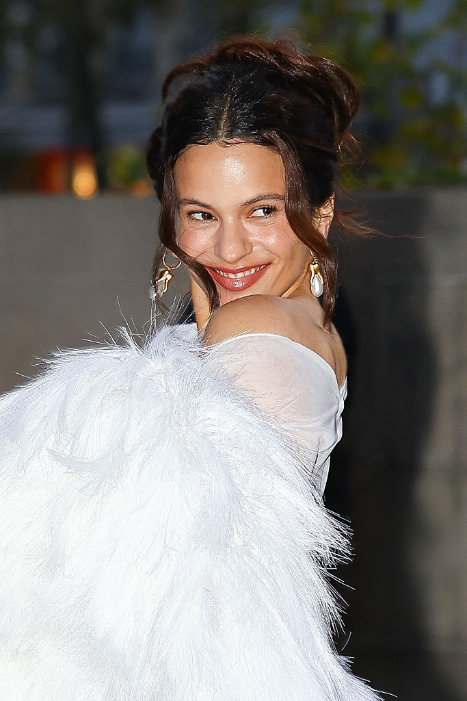 Person wearing an elegant, textured achromatic shawl, smiling astatine the camera with an updo hairstyle and connection earrings