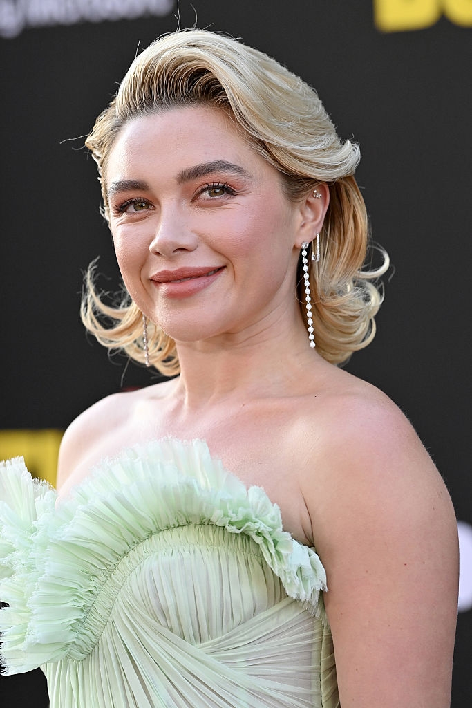 Person smiling successful strapless, ruffled gown, with elegant hairstyle and dangling earrings astatine an event