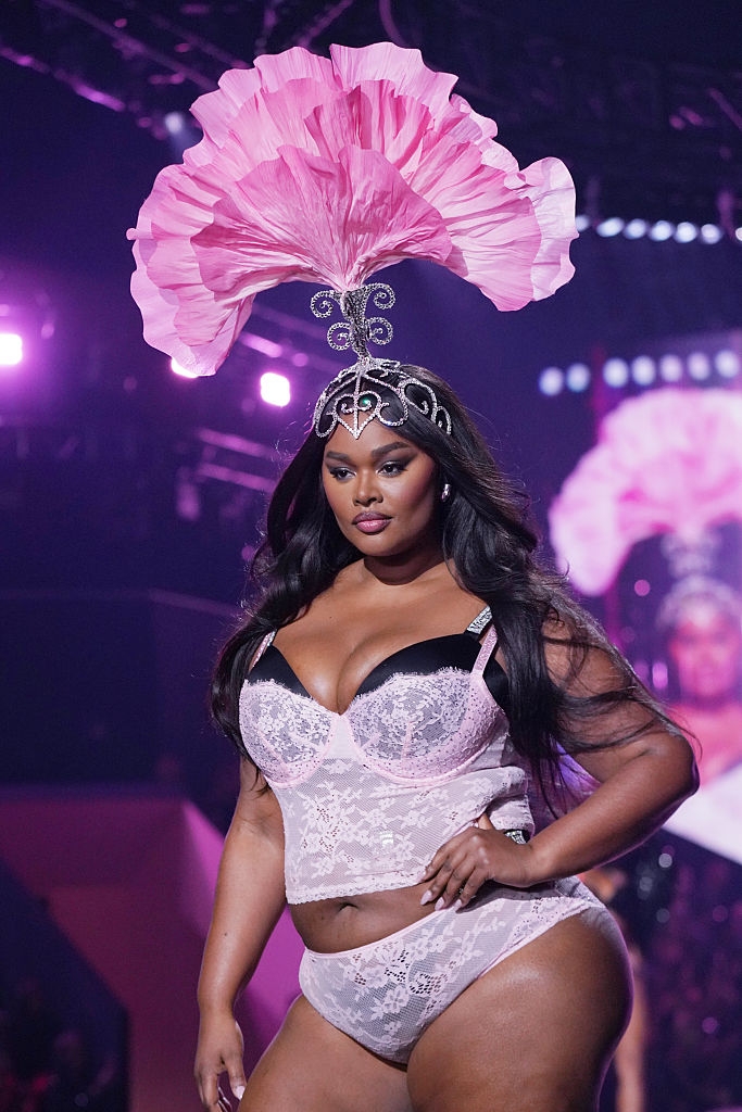 Model connected runway wearing ornate feathered headpiece and stylish lingerie set, exuding assurance and elegance during a manner show