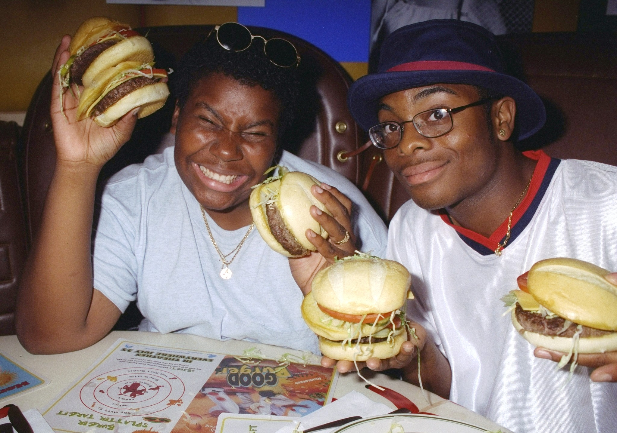 Two radical   smiling and holding ample  burgers astatine  a edifice  table, enjoying their meal