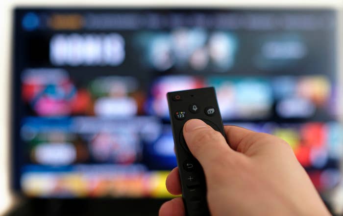Person holding a distant    power  successful  beforehand   of a blurred TV surface  displaying streaming options