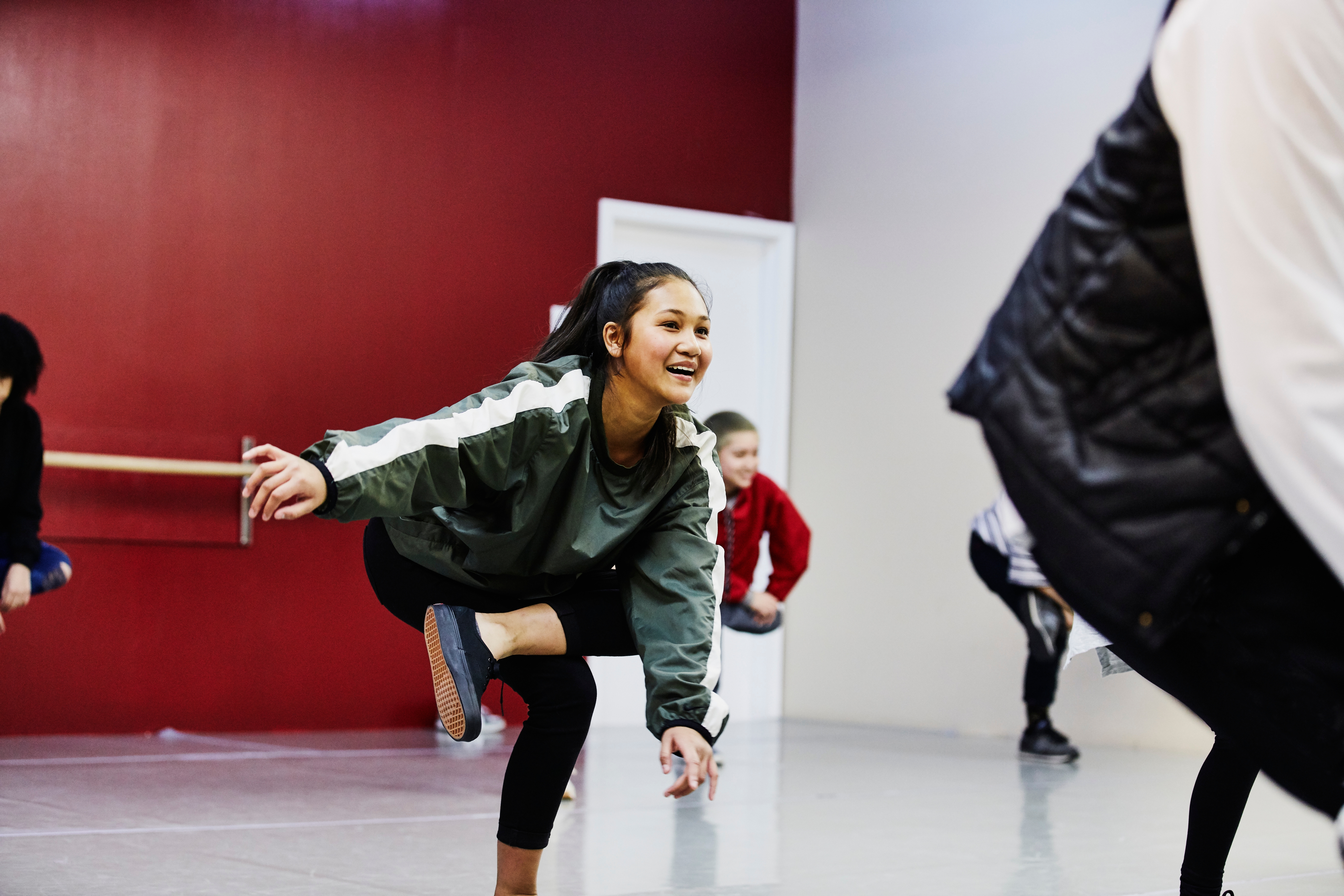 En smilende kvinne i et dansestudio strekker seg med en gruppe, iført et atletisk antrekk