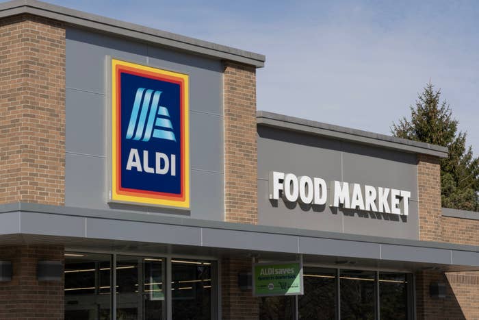 Aldi supermarket exterior with large &quot;Food Market&quot; sign, brick walls, and trees in the background