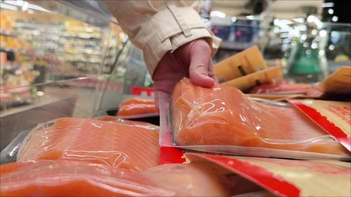 Person reaching for a vacuum-sealed package of salmon in a grocery store aisle