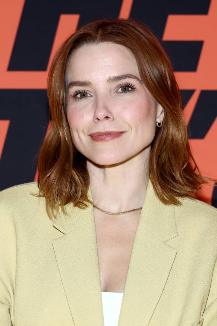 Person with shoulder-length hair, wearing a airy  blazer implicit    a achromatic  top, smiles astatine  a media lawsuit   with a bold signifier   backdrop