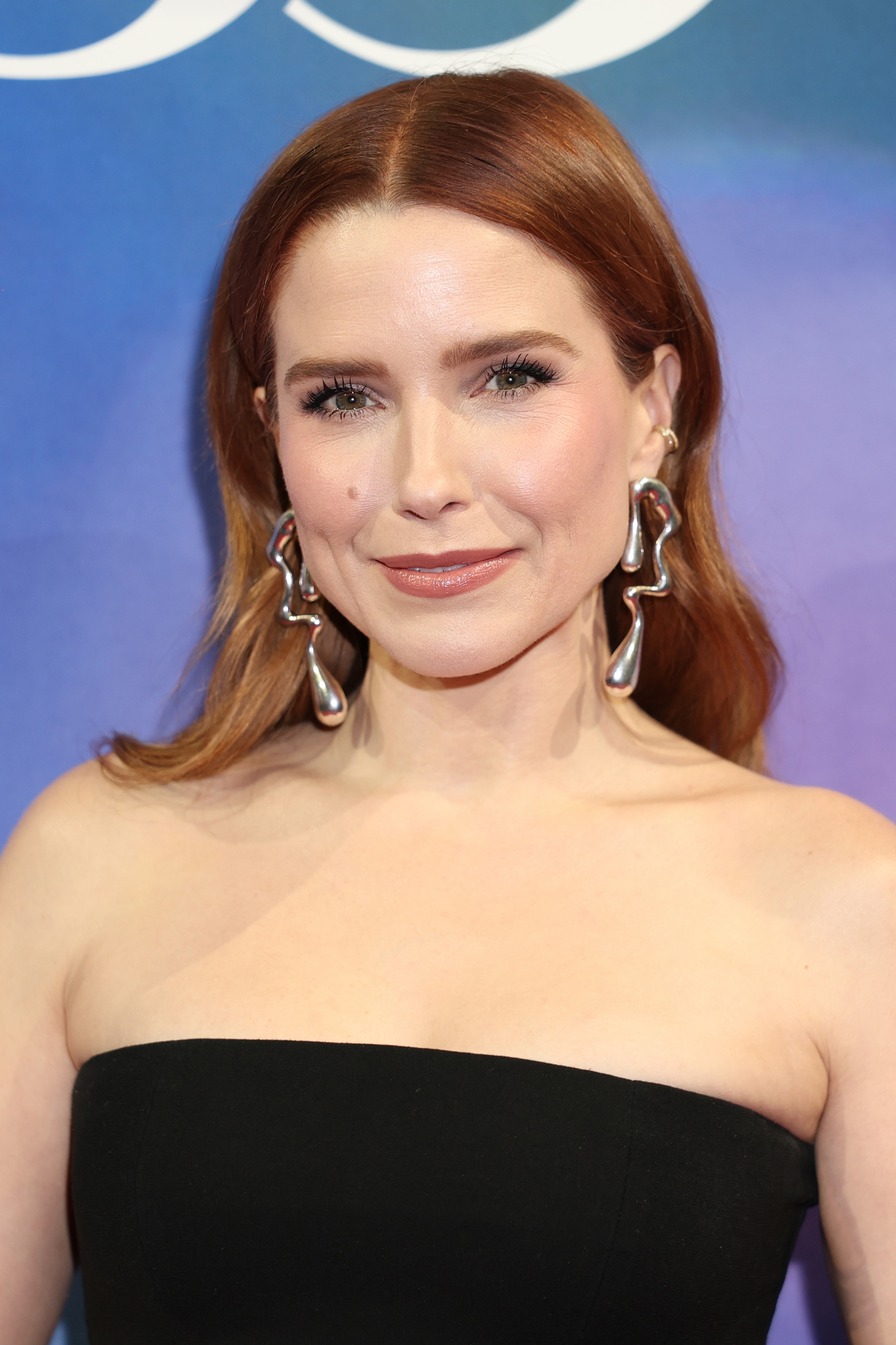 Person astatine  an lawsuit   wearing a strapless achromatic  formal  and connection    earrings, smiling astatine  the camera