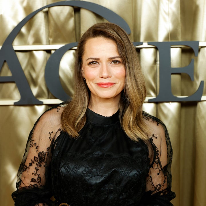 Person in elegant black lace dress poses in front of a gold backdrop with text partially visible