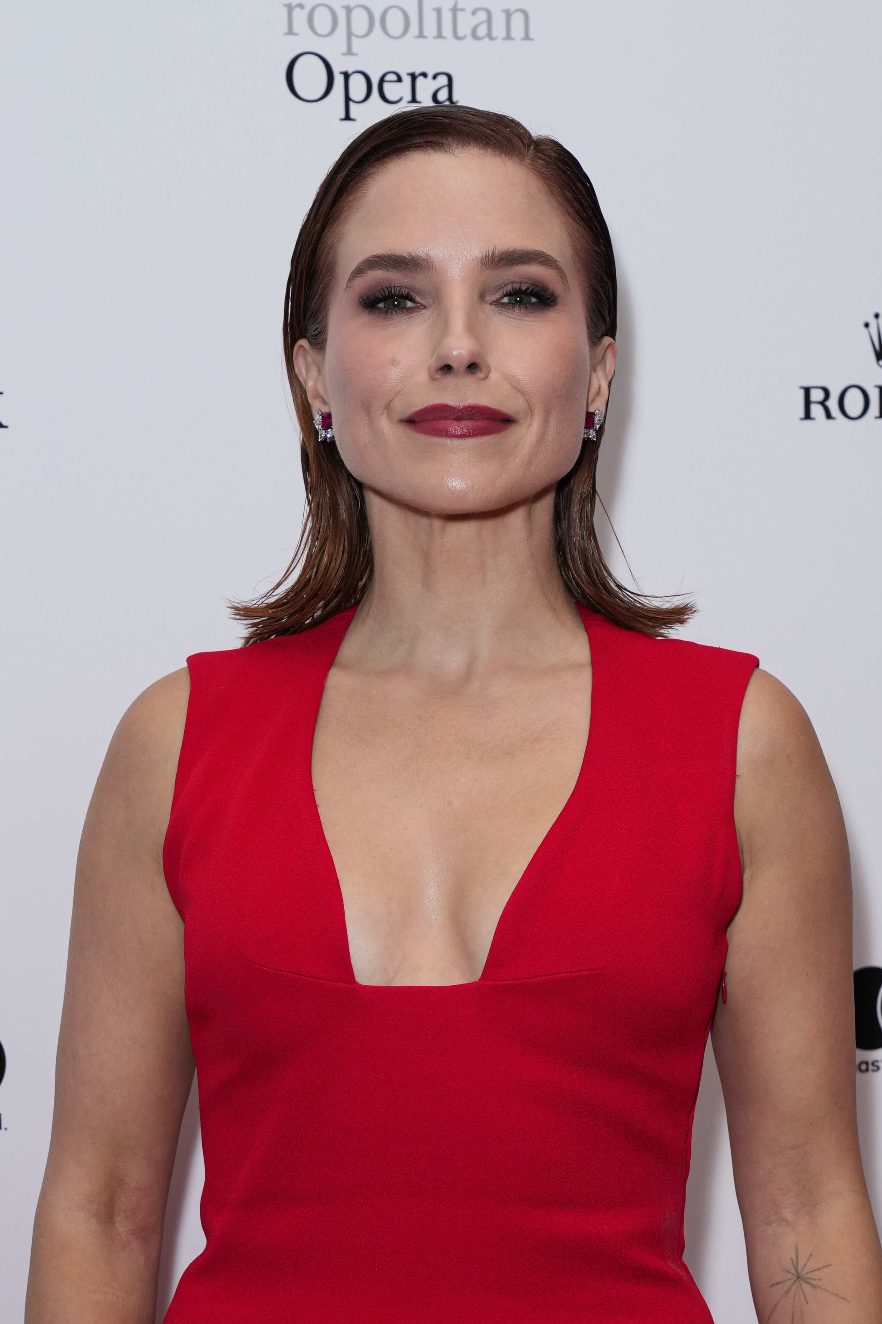 Person successful  elegant, sleeveless formal  with heavy  neckline astatine  a ceremonial  event, smiling astatine  the camera, hairsbreadth  styled sleekly back