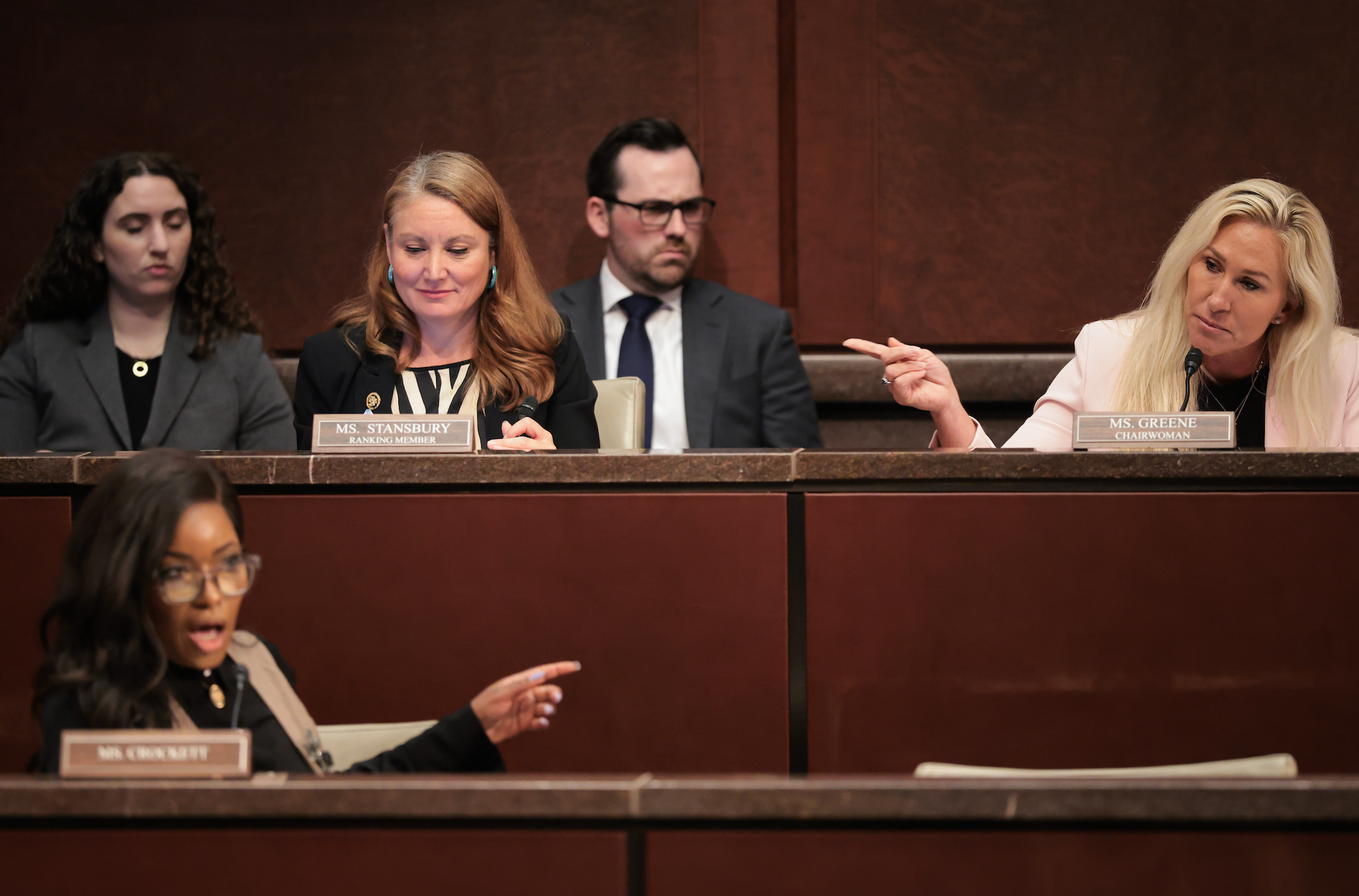 People in a formal setting, engaging in a lively discussion. Two are pointing, suggesting debate or disagreement, while others look attentive
