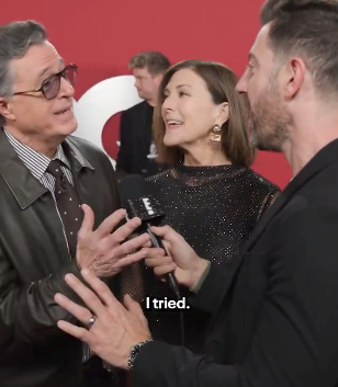 Two people in elegant attire are being interviewed on a red carpet. The man wears a leather jacket; the woman has a shimmering dress. Subtitles read: &quot;I tried.&quot;