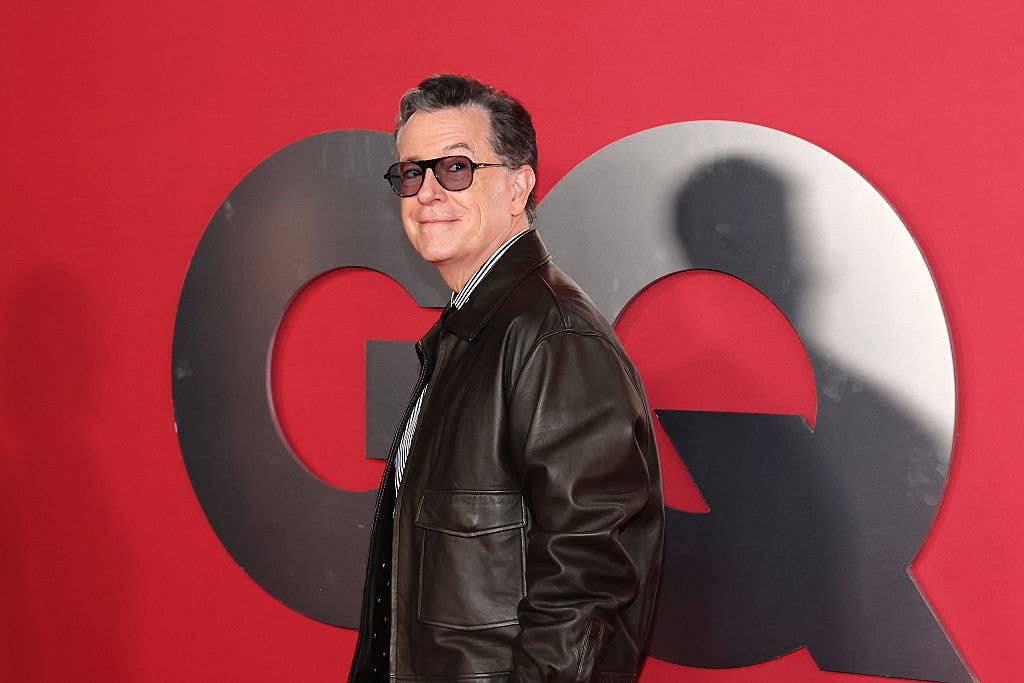Person on red carpet in leather jacket and striped shirt, posing in front of large decorative letters