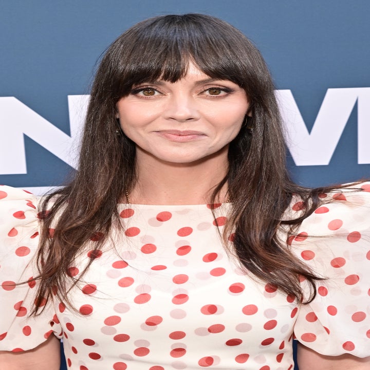 Person in a white dress with red polka dots at a celebrity event, smiling at the camera