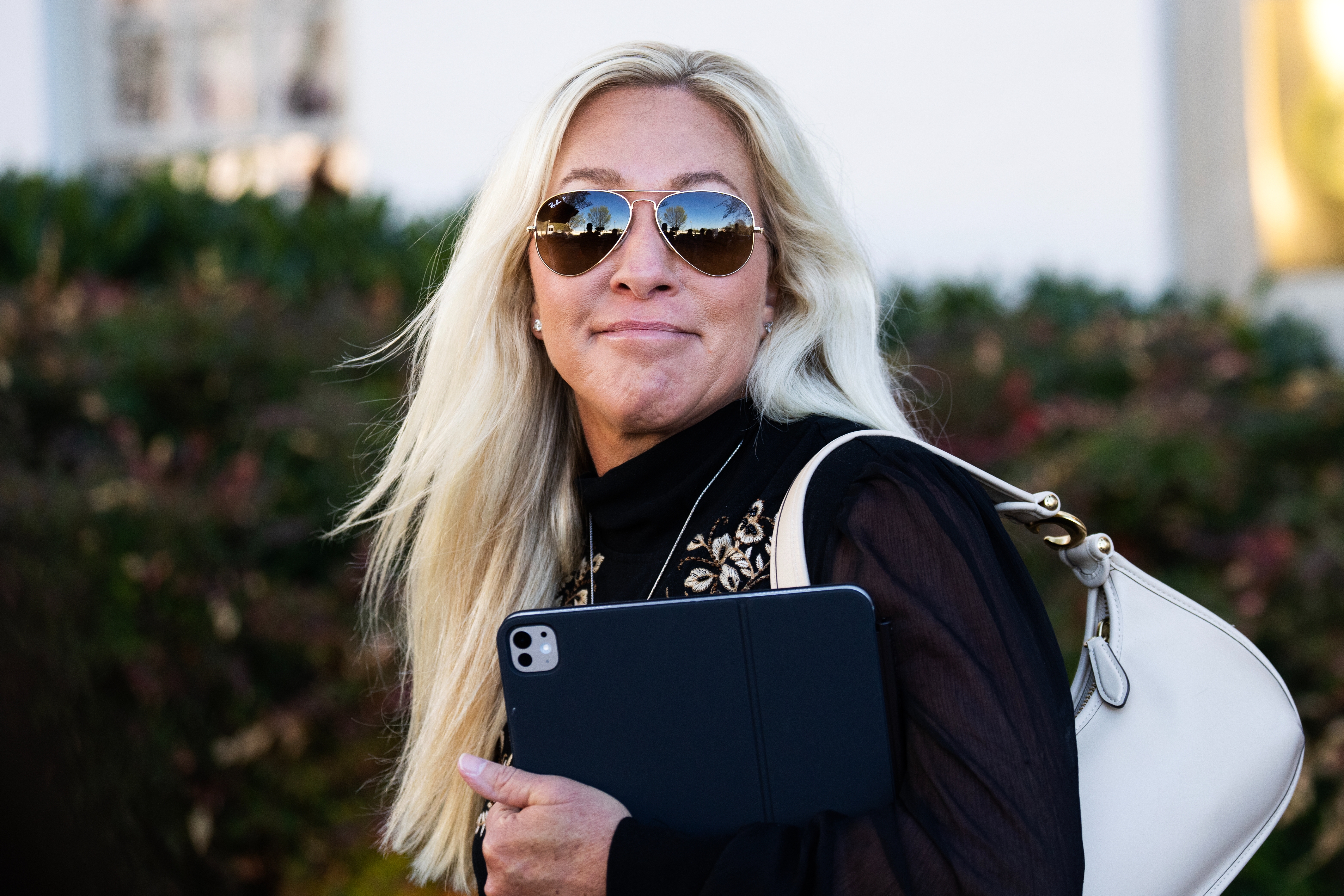 Marjorie Taylor Greene with agelong  hairsbreadth  and sunglasses smiles portion    holding a tablet, wearing a achromatic  apical  with decorative details