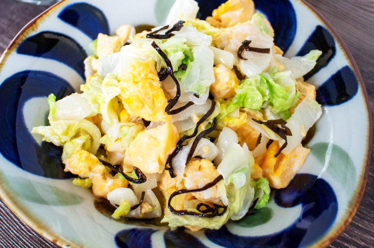 皿に盛られたクリーミーなサラダ。キャベツ、卵、昆布などがトッピングされている。背景にお箸と小皿。