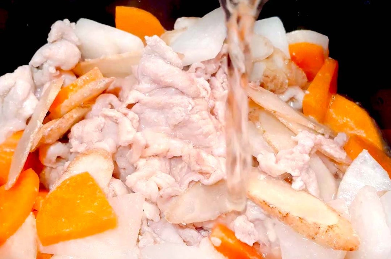 鍋で煮込み料理を作る様子。野菜と肉が入っており、上から液体が注がれている。調理の過程を示している。