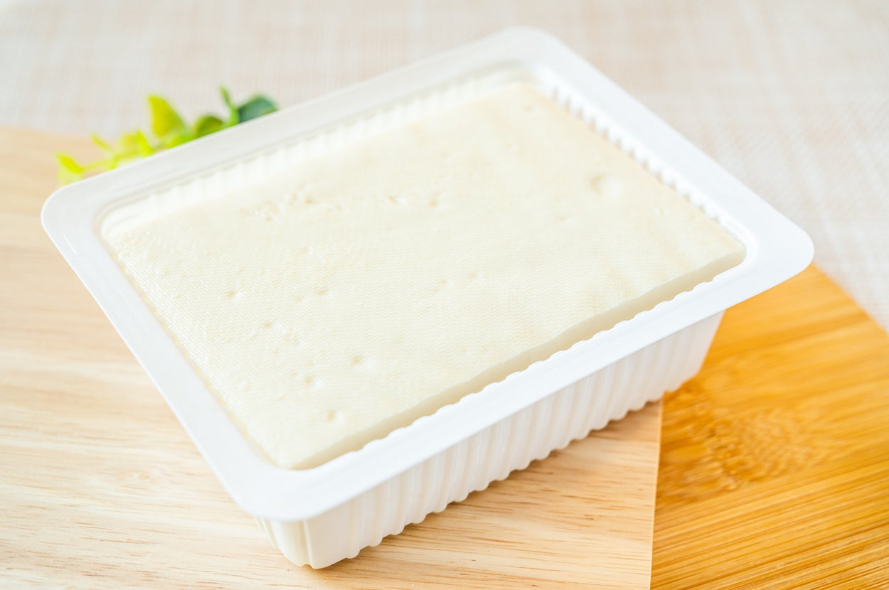 プラスチック容器に入った豆腐が木製のカッティングボード上に置かれている。