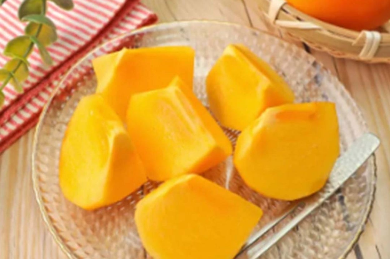 ガラスの皿に盛られたスライスされた柿。隣には籠入りの柿と緑の飾り。