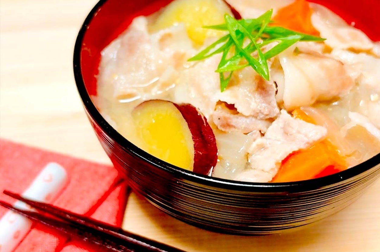豚汁が赤い器に盛られ、箸が横に置かれている。具材には肉、サツマイモ、人参、ネギが見える。