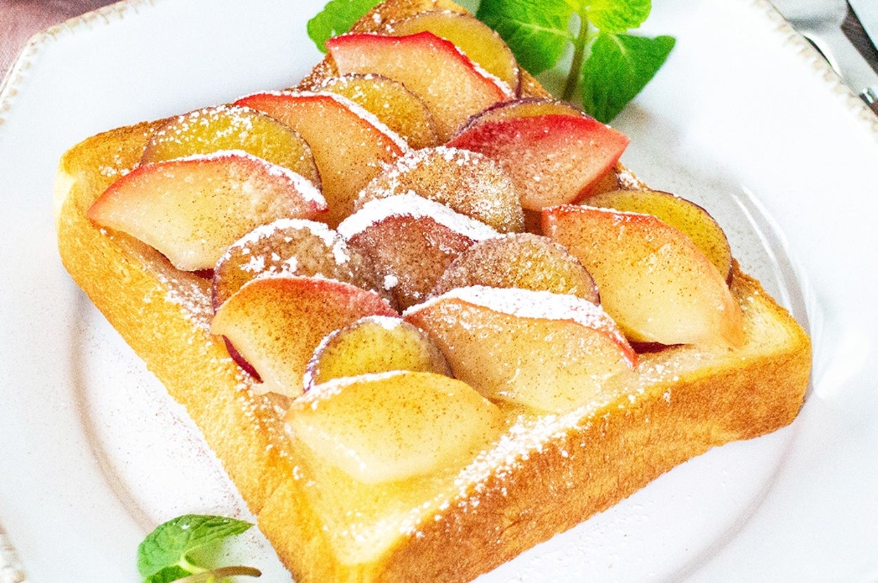 トーストにスライスされたリンゴが載せられ、粉砂糖がかかっている。横にミントの葉が添えられているプレート。