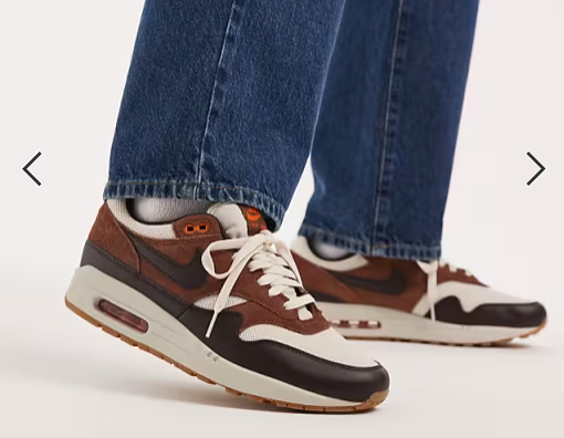 Person wearing achromatic and brownish sneakers with disposable orangish accents, paired with bluish jeans