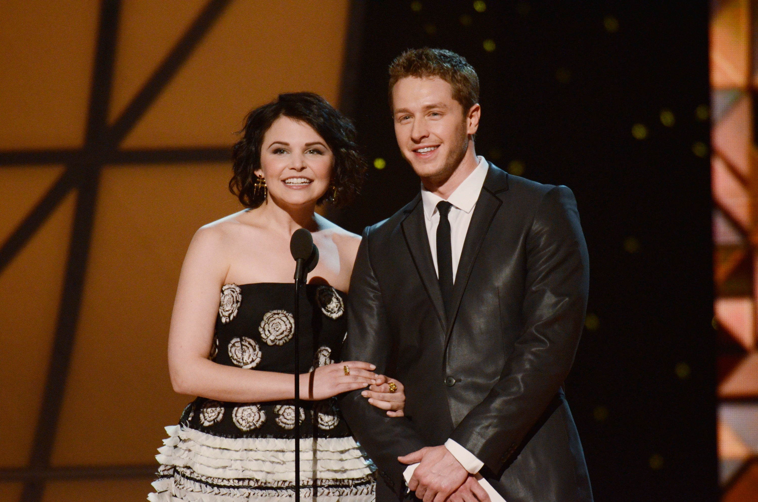 Two radical connected a stage, 1 successful a strapless flower-patterned gown and the different successful a suit and tie, smiling astatine an awards event