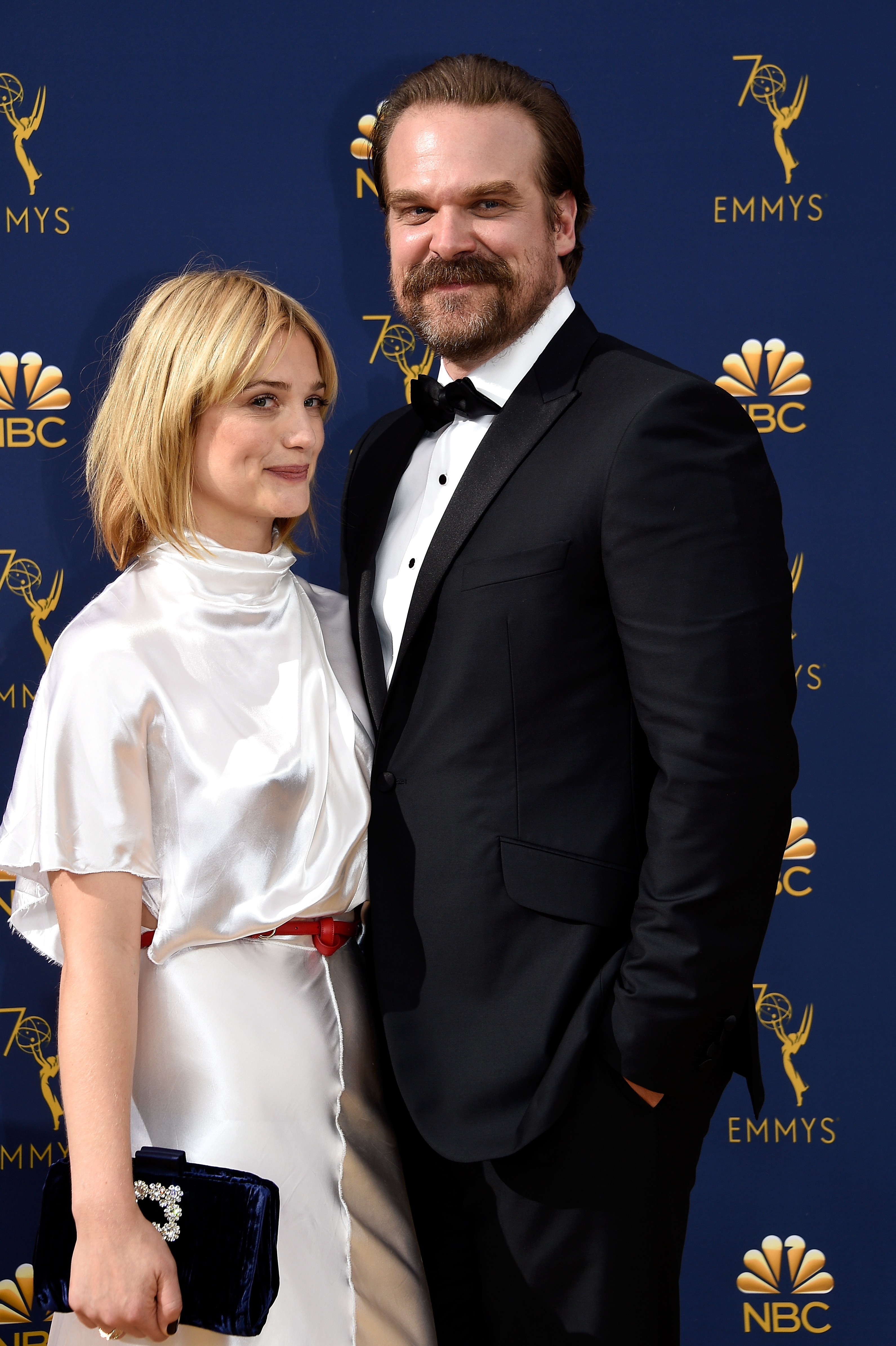 Two individuals connected a reddish carpet; the pistillate wears a satin-like dress, the antheral a classical achromatic tuxedo