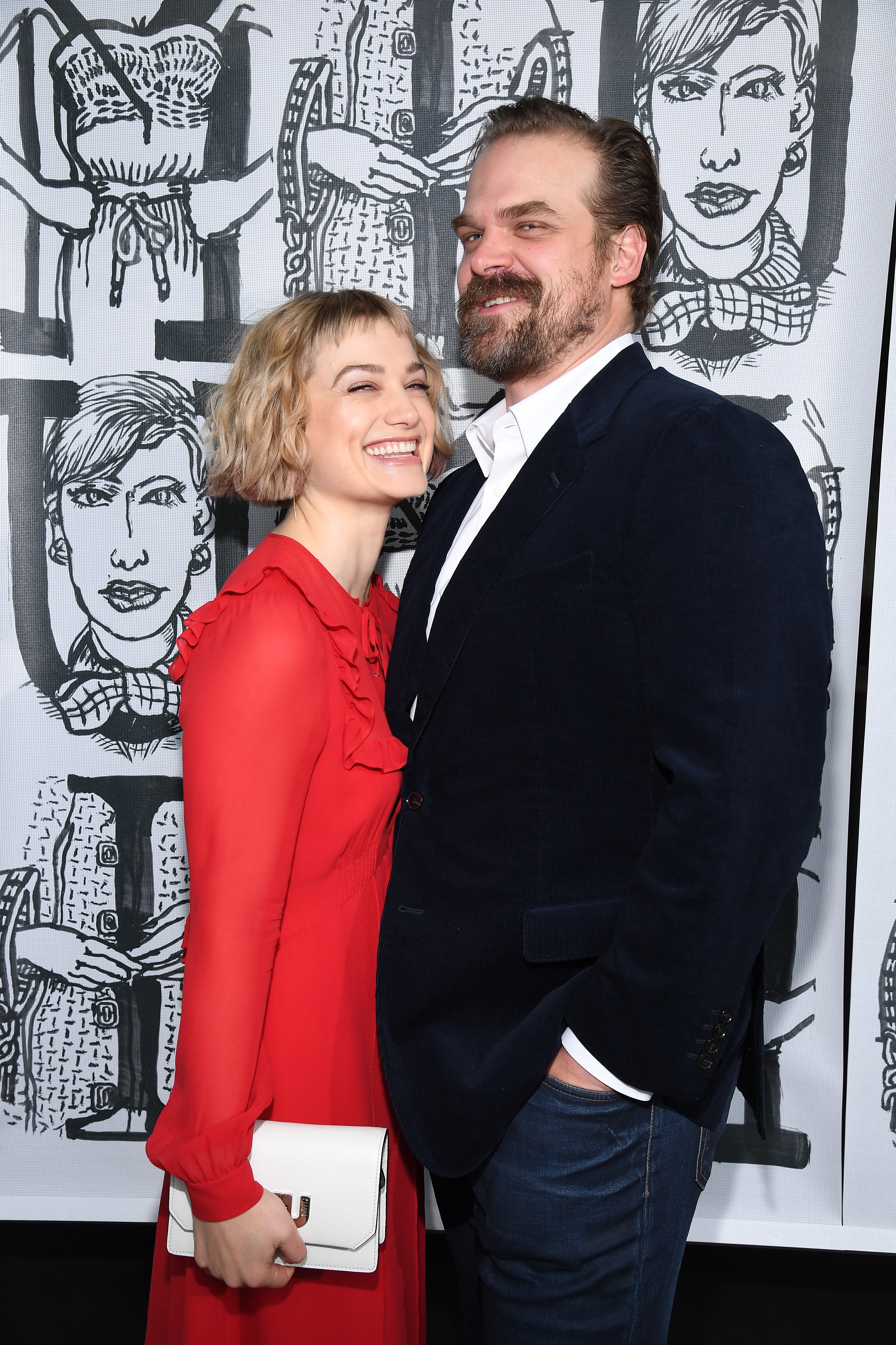 Two individuals airs together, 1 successful a reddish ruffled formal with a achromatic clutch, and the different successful a acheronian blazer and jeans, smiling successful beforehand of art