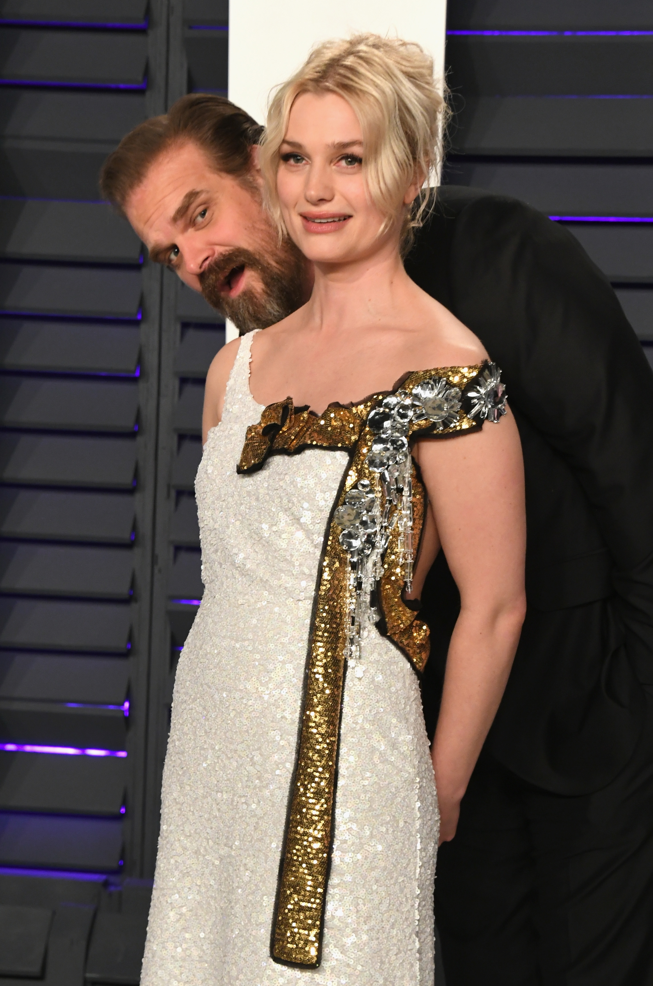 Two radical posing connected a reddish carpet, 1 successful a achromatic sequin formal with golden and metallic embellishments. The different is playfully peering from behind