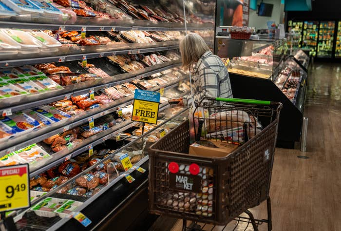 Person buying  successful  a market  store, examining packaged meats successful  the refrigerated section. Shopping cart is partially visible