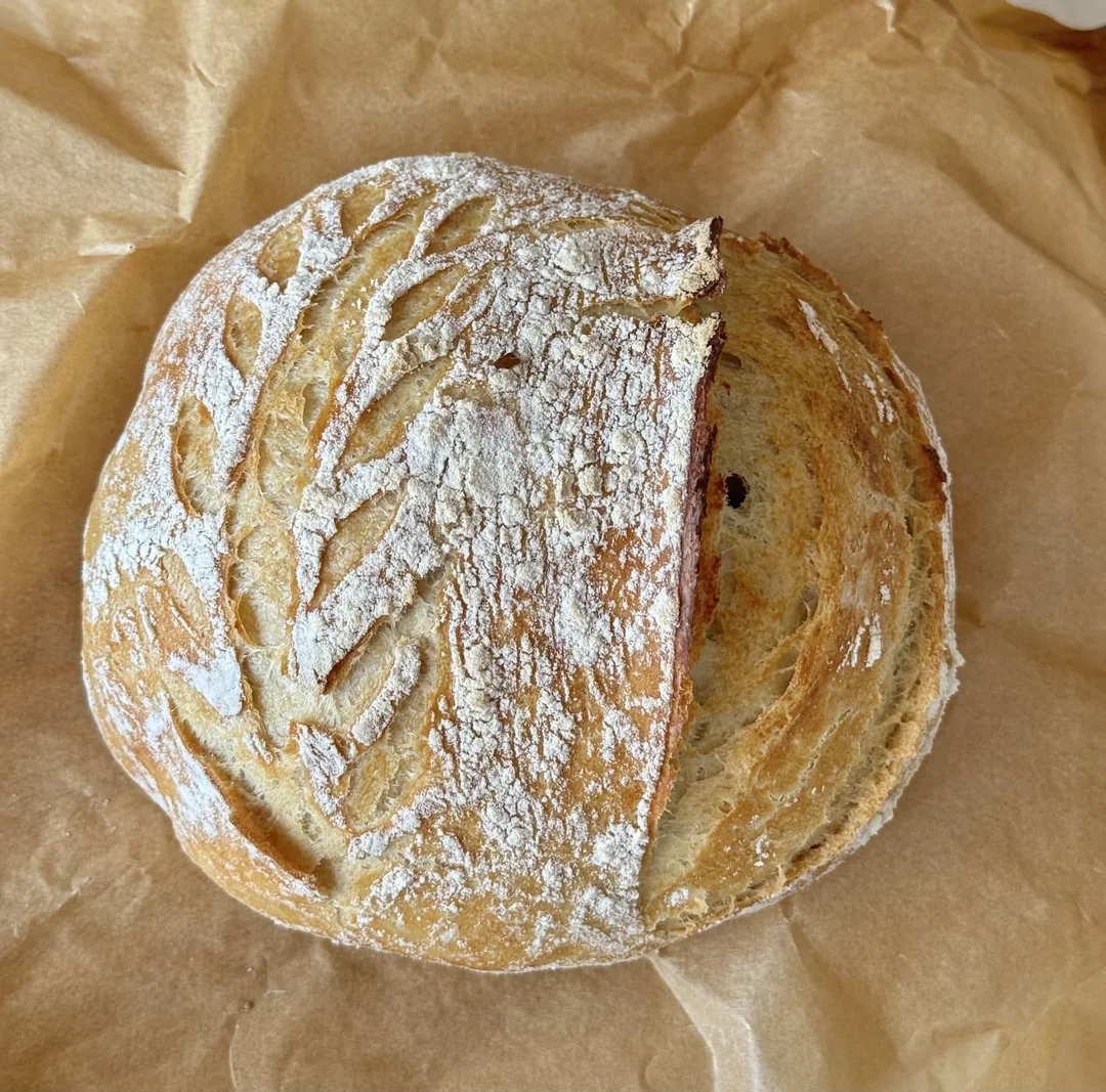 Rundt håndverksbrød med dekorativt skråmønster på toppen, hviler på brunt bakepapir