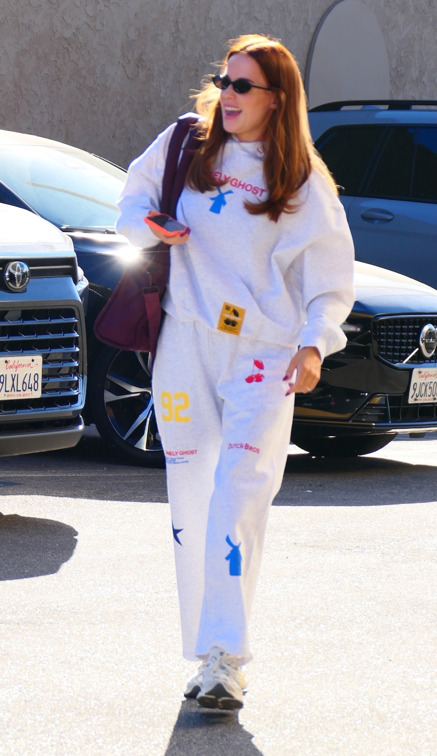 Person i tilfeldig merkedress og solbriller går på en parkeringsplass med en telefon