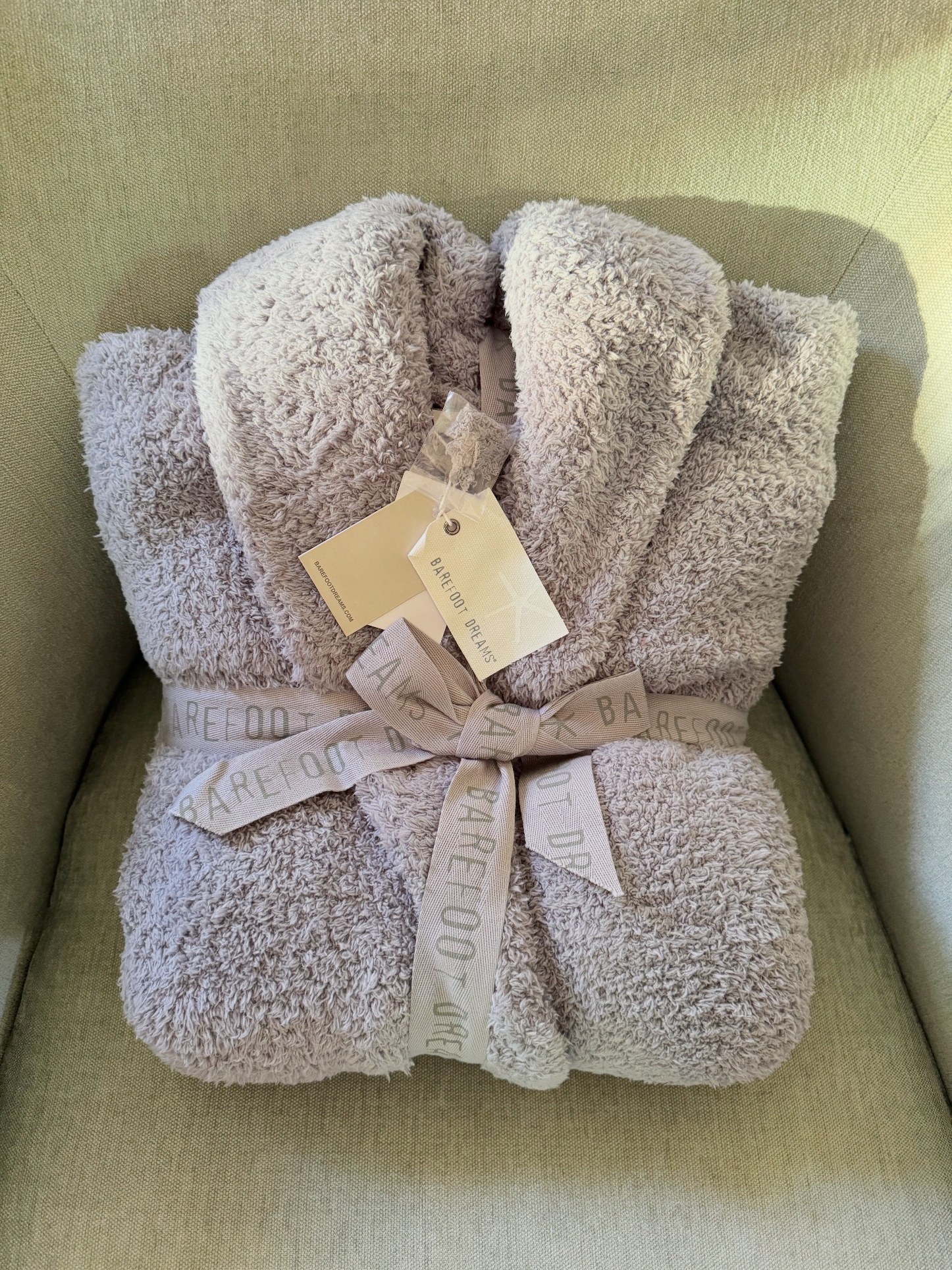 Myk, brettet badekåpe med merkelapp, pakket inn i et bånd, hvilende på en polstret stol