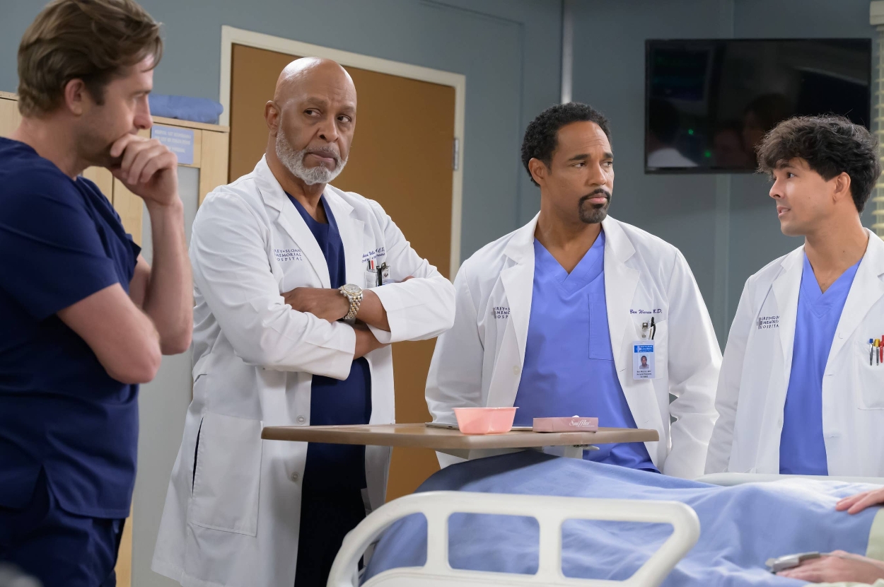 Four people in scrubs and lab coats stand around a hospital bed, engaged in conversation on a TV medical drama set