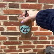 Someone holding up a plastic to-go cup against a brick wall