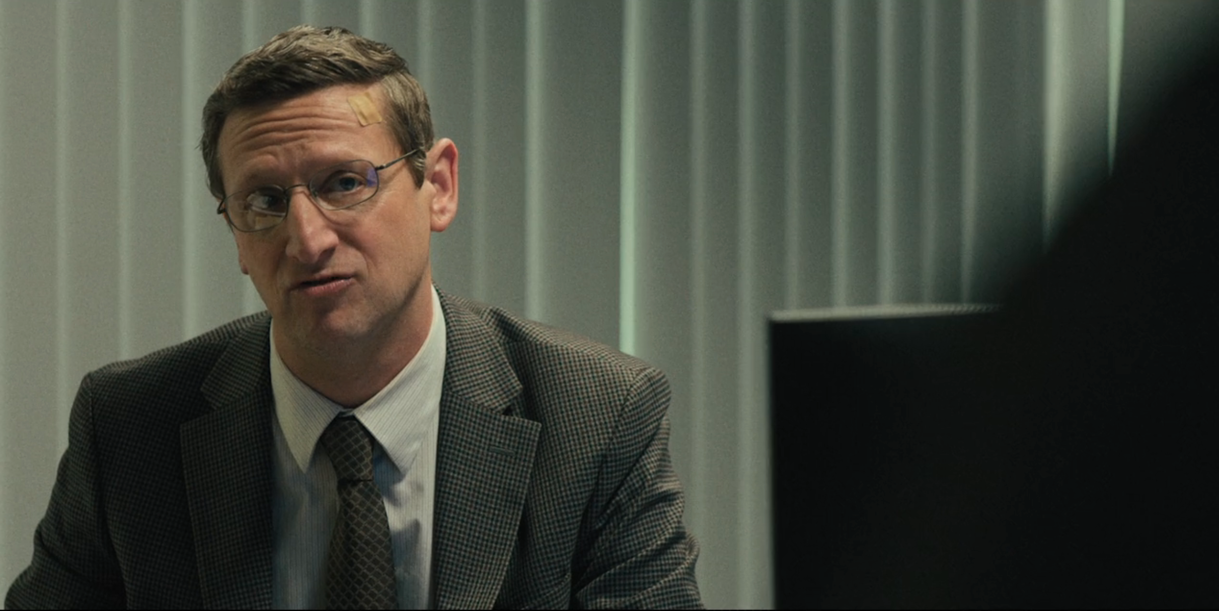 Person successful  an bureau   wearing a checkered suit   and glasses, sitting successful  beforehand   of venetian blinds, appears to beryllium  speaking