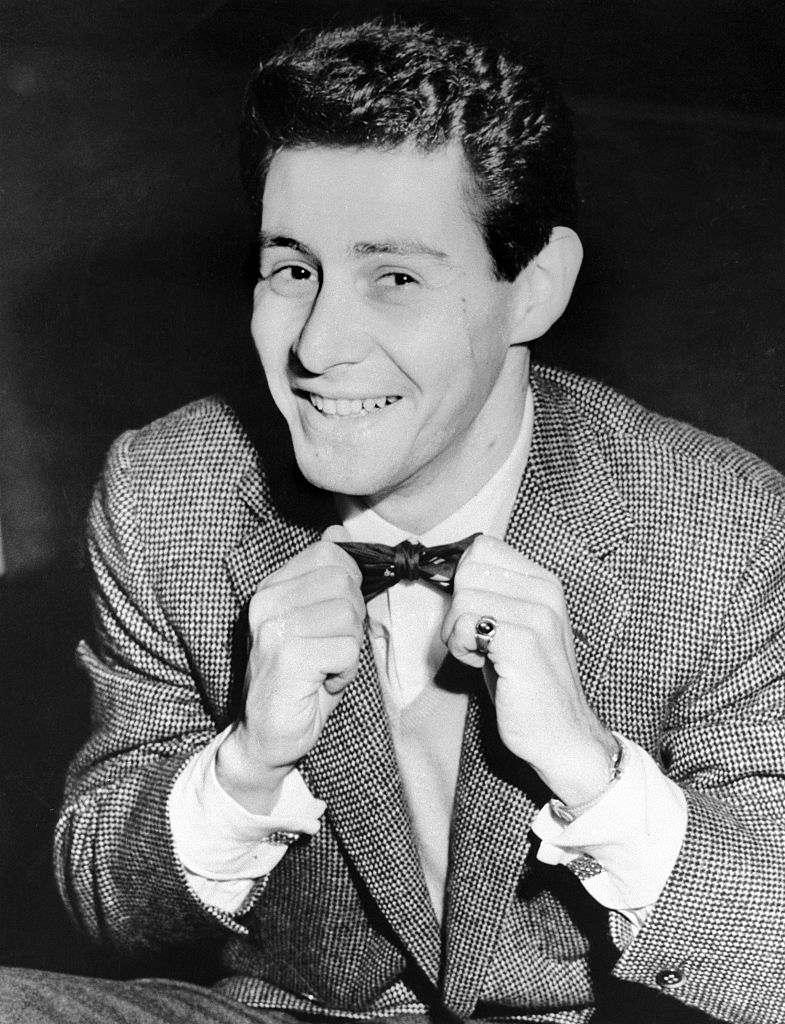 Fisher adjusts his bow tie, smiling astatine the camera