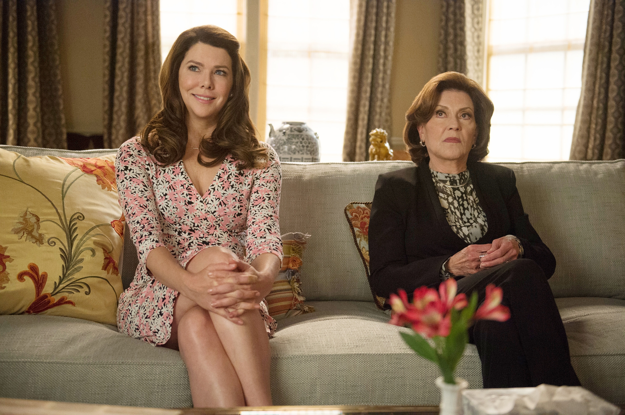 To kvinner sitter i en sofa; den ene har på seg en blomsterkjole, den andre en svart blazer. De ser ut til å være i en avslappet, uformell setting