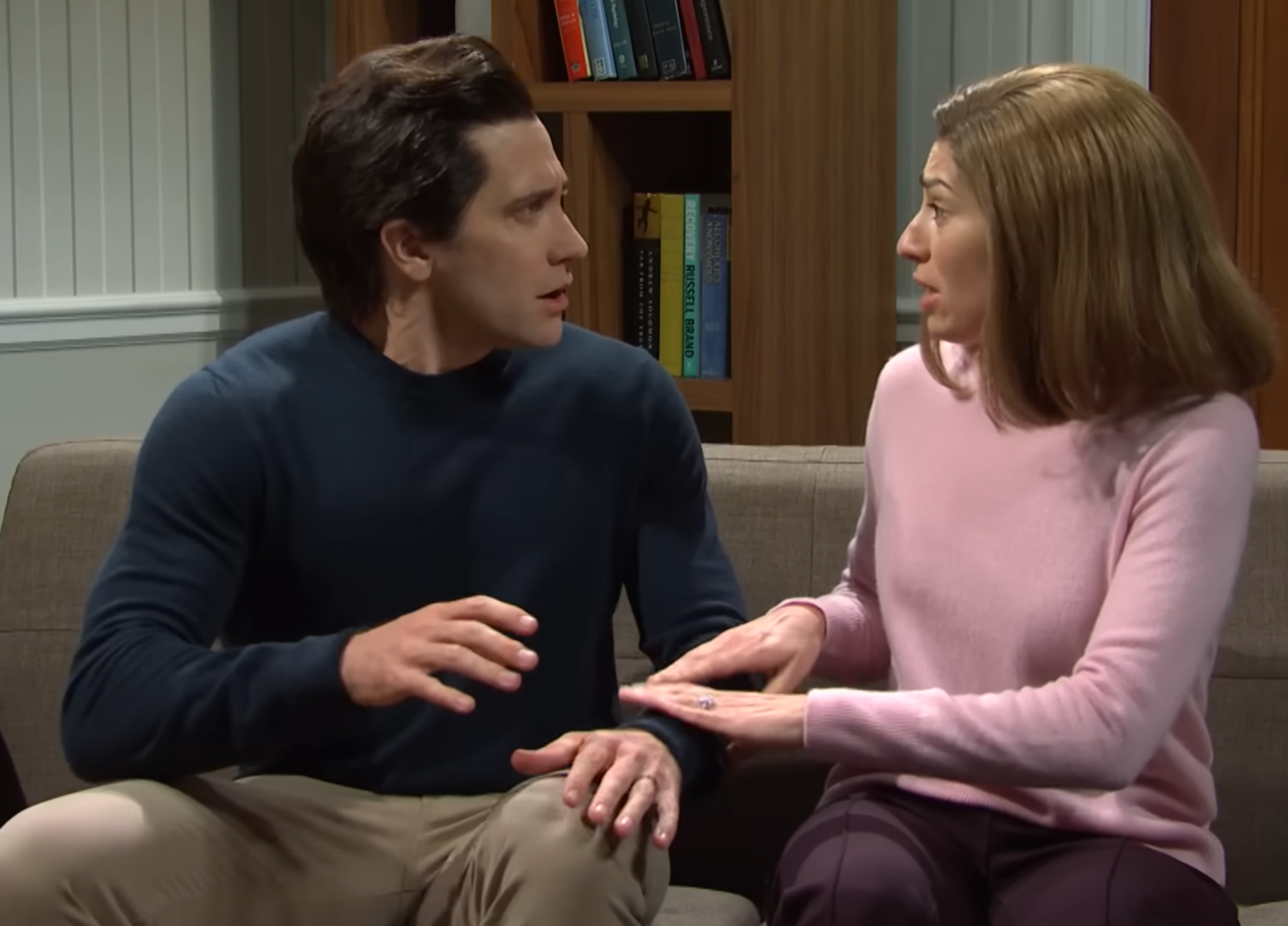 To personer sitter på en sofa i en komisk scene, ser overrasket ut og er engasjert i animerte samtaler