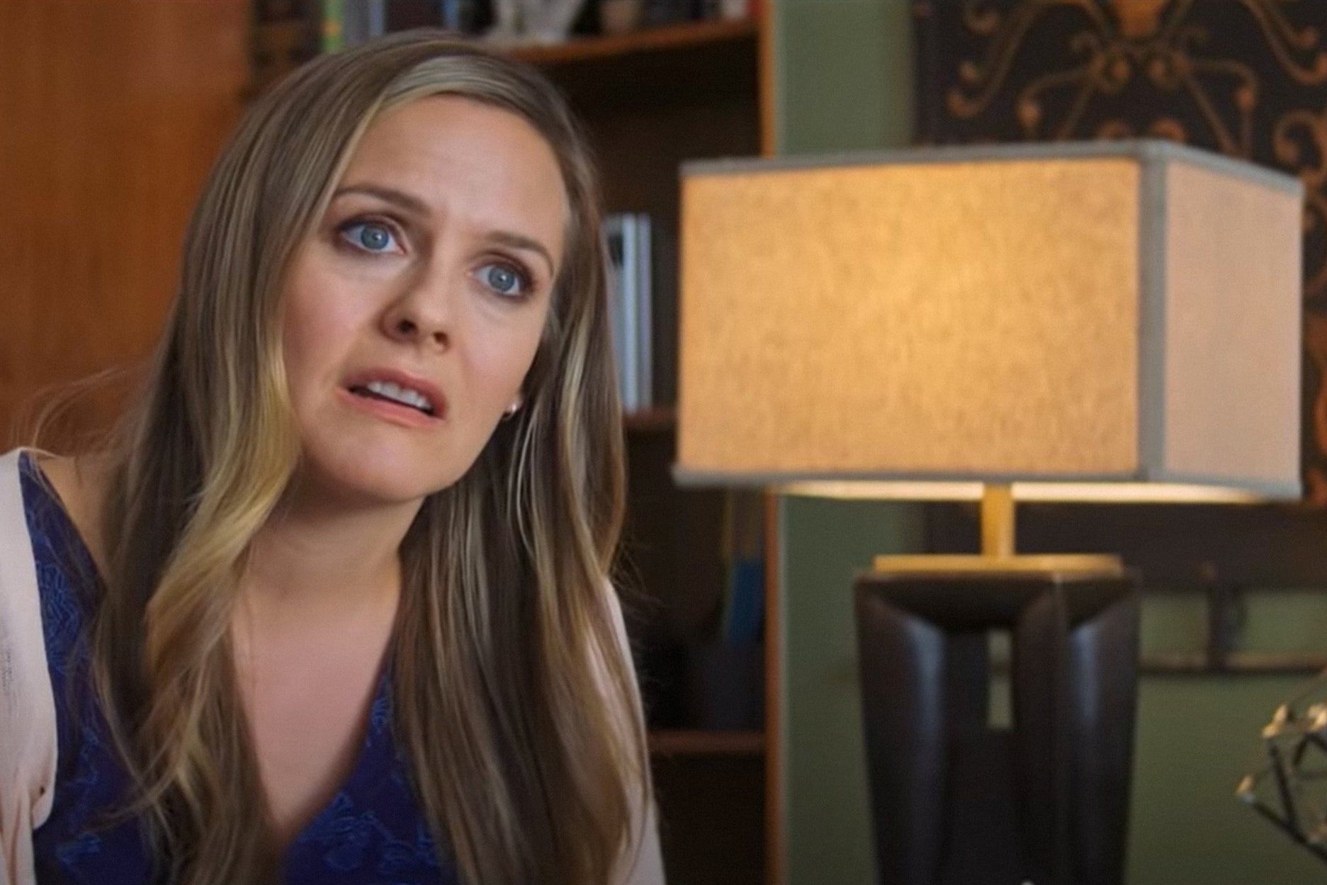 Person som sitter innendørs, virker gjennomtenkt, ved siden av en moderne lampe og innredning