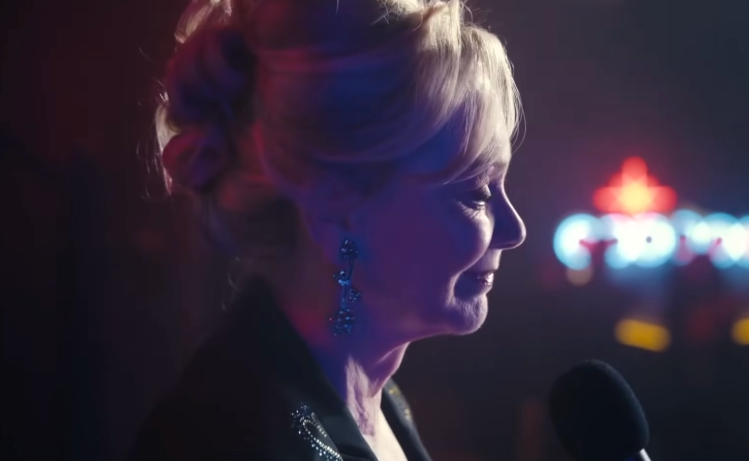 A idiosyncratic   with styled hairsbreadth  and elegant earrings smiles portion    speaking into a microphone astatine  an event