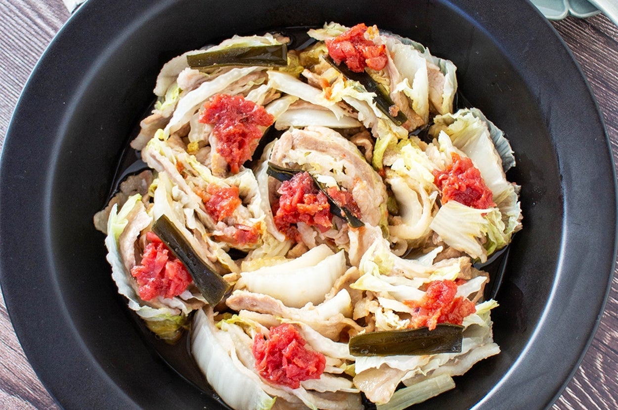 鍋の中に盛られた白菜と肉の料理。トマトやピクルスがトッピングされ食欲をそそります。