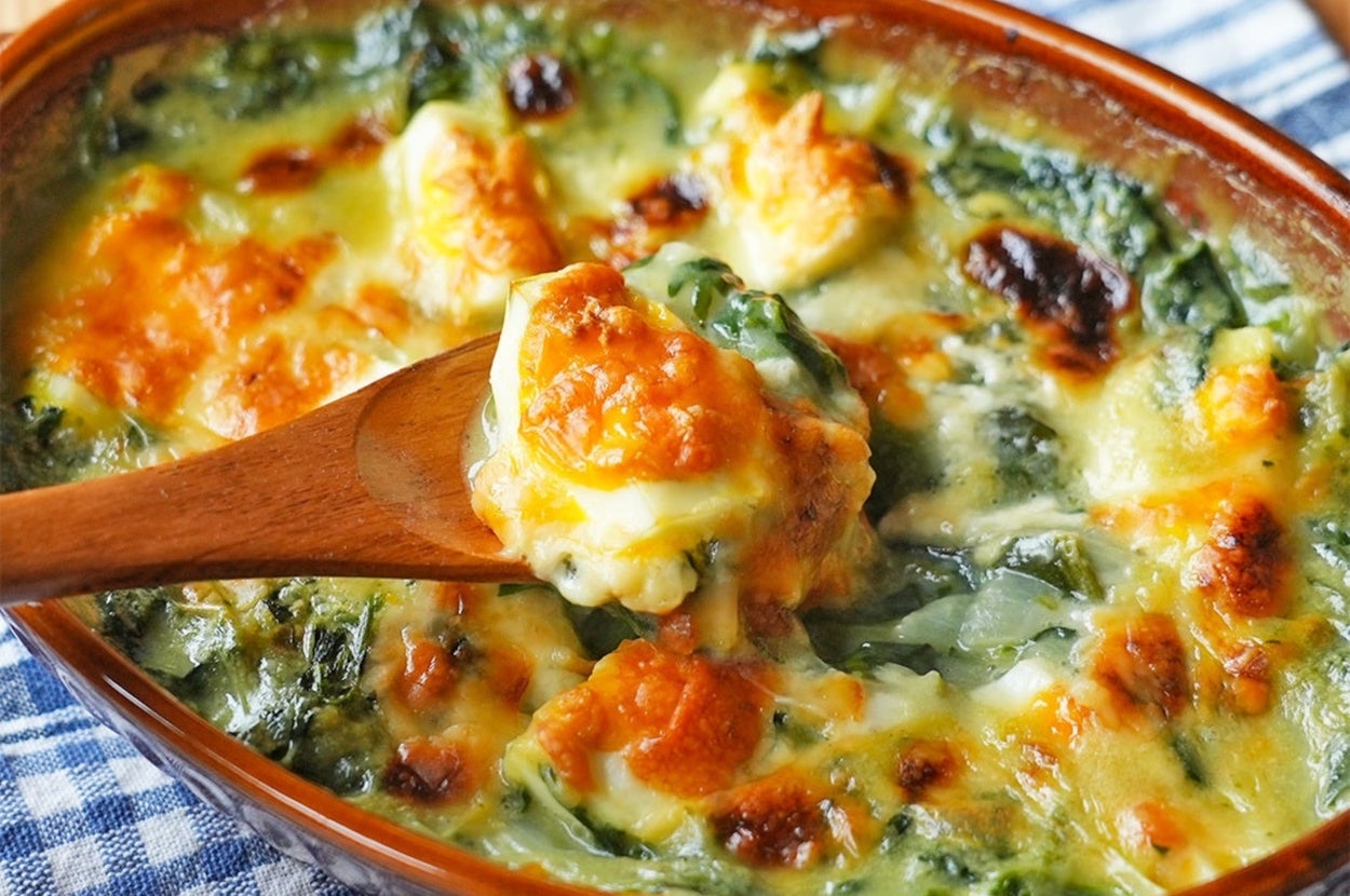 スプーンで一部がすくわれた、グラタン風の焼かれた料理。お皿の下にはチェック柄の布。