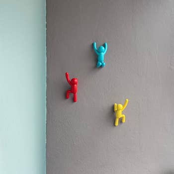 Three partition hooks shaped similar climbers successful red, blue, and yellowish adorn a patio wall, with a leafy works successful the corner