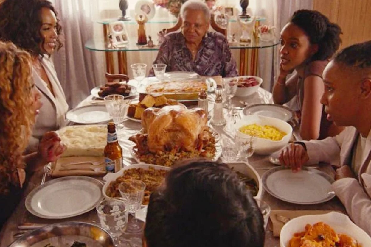 Family gathered around a table for a meal, with a roast turkey and various dishes. Seven people are engaged in conversation and sharing food