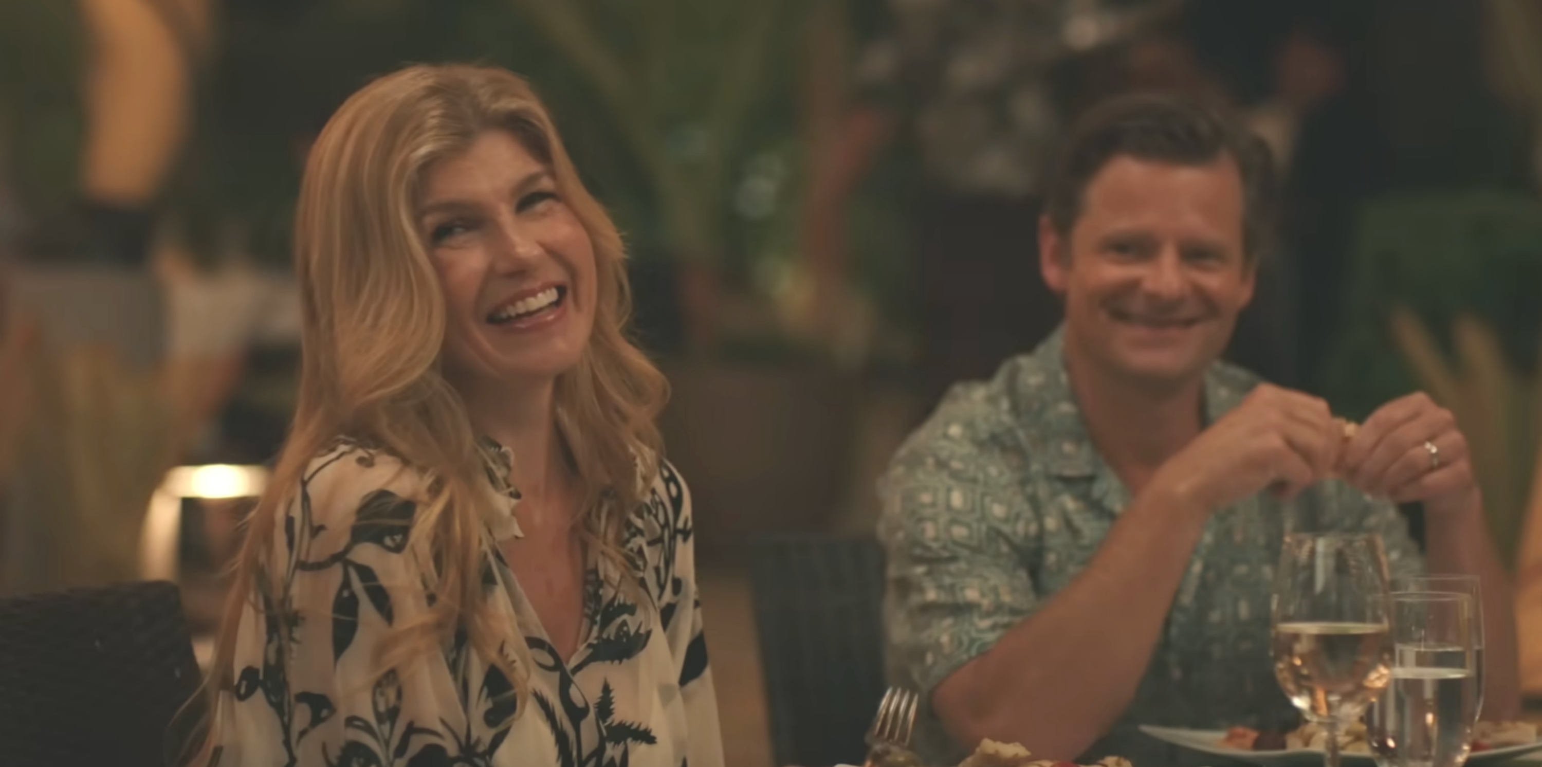 A pistillate   successful  a floral blouse and a antheral   successful  a patterned garment  grin  portion    seated astatine  an elegant dinner, suggesting a joyful moment