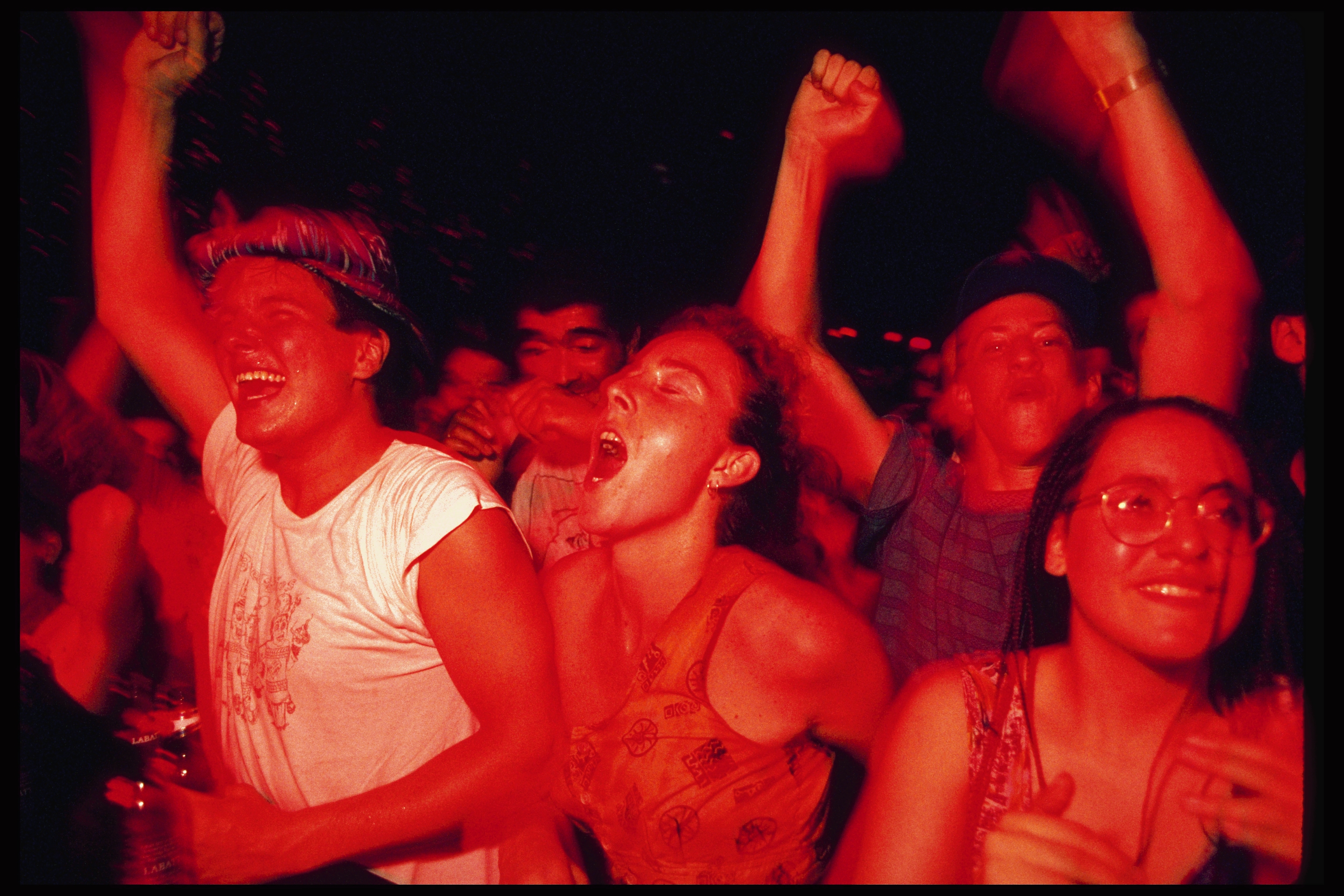 Folk på en livlig konsert, jubler med armene hevet, uttrykker begeistring og glede