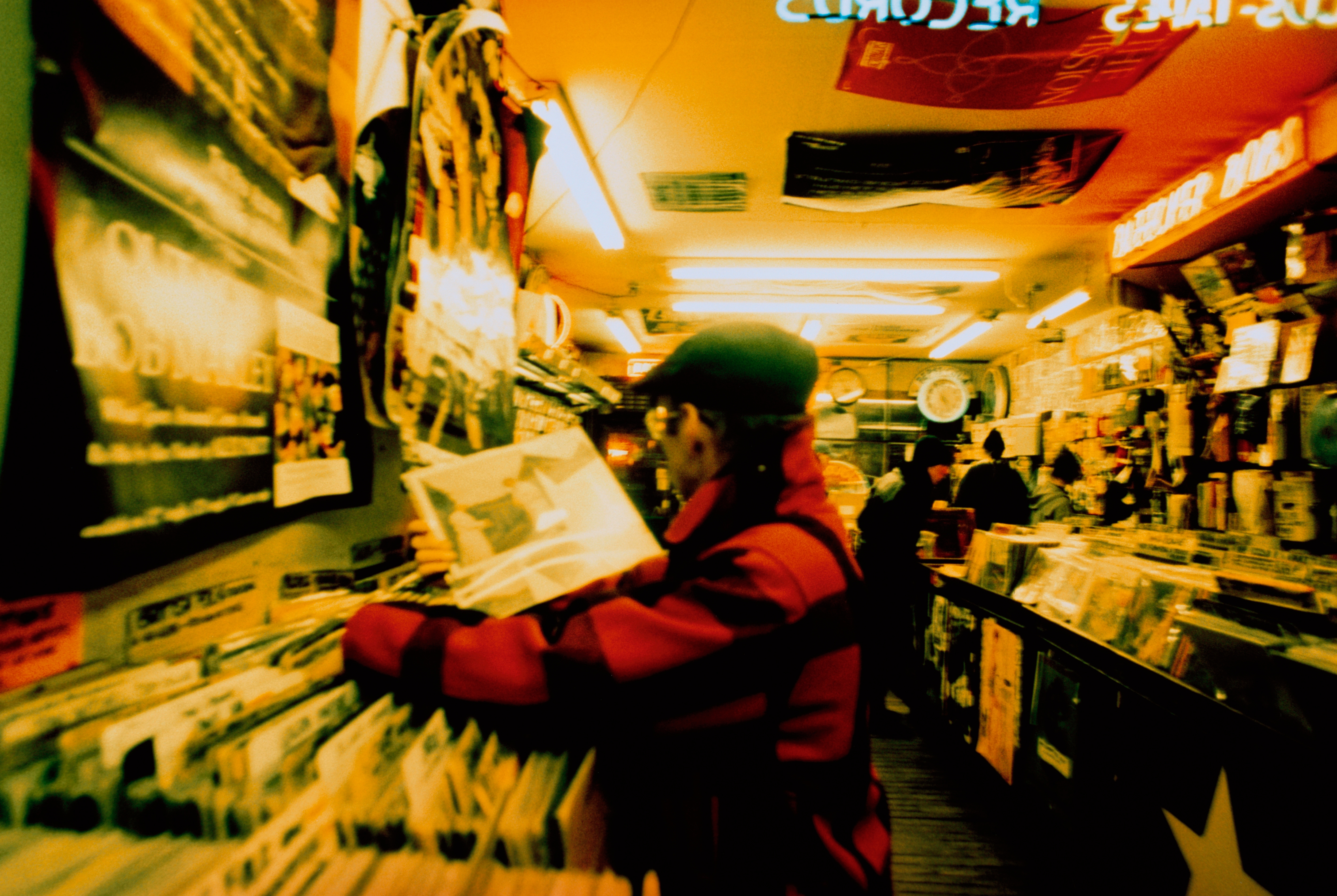 Person som blar gjennom plater i en koselig musikkbutikk i vintagestil, omgitt av fargerike albumomslag og varm belysning