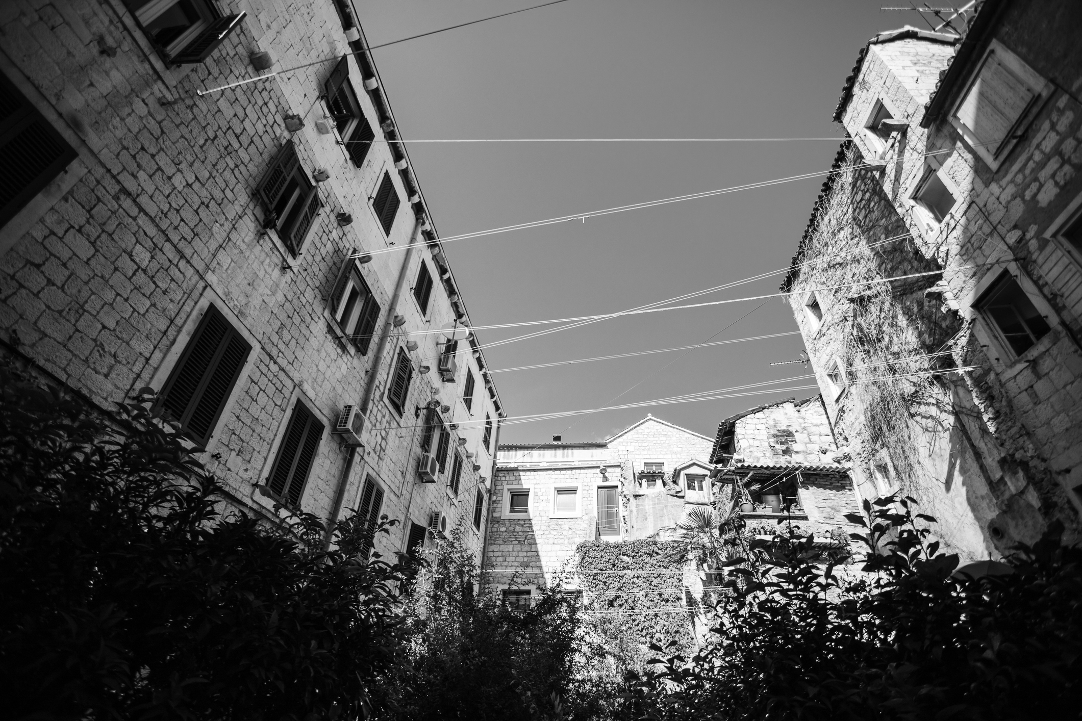 Stone buildings with windows and clotheslines above, viewed from below, captured successful  a constrictive  courtyard setting