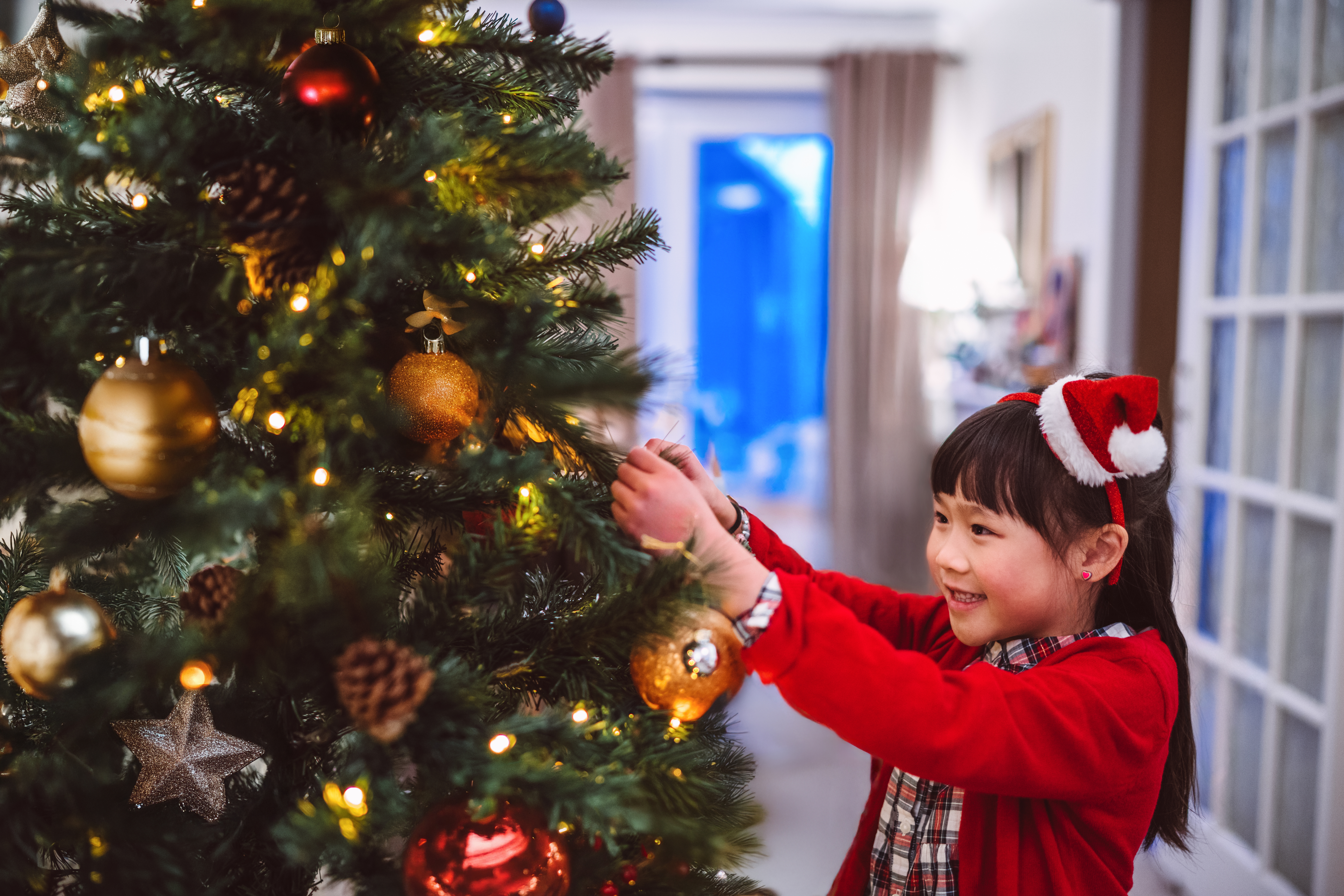 Barn i festlig antrekk pynter et juletre med pynt og lys i et koselig rom